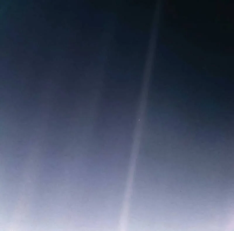 A foto mostra um grande plano azul com um pequeno ponto, a Terra, bem claro.